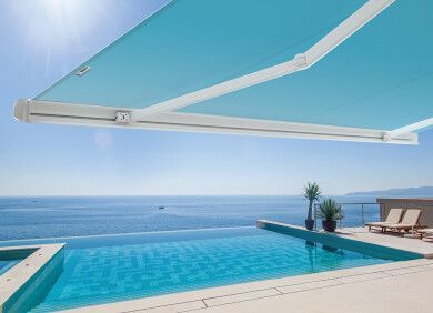 Piscina a sfioro con vista sull'oceano, protetta da una tenda da sole retrattile blu.