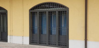 Facciata gialla dell'edificio con cancello ad arco in metallo grigio e finestre con sbarre.