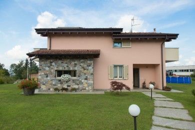 Casa beige a due piani con facciata in pietra, tetto rosso e prato con sentiero in pietra e lampione.