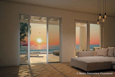 Tramonto visto attraverso le porte finestre aperte che danno su un moderno soggiorno con divano bianco e vista sull'oceano.