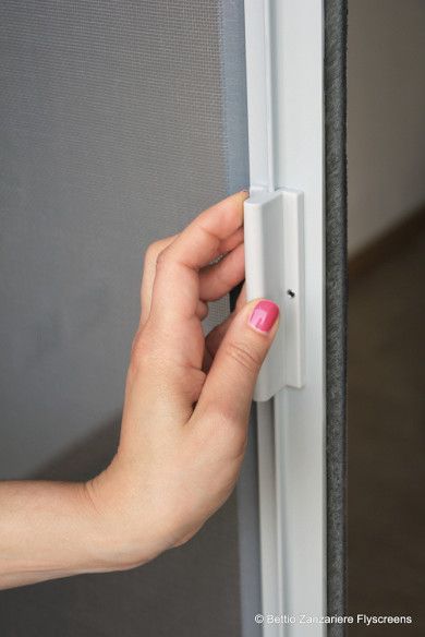 Mano che apre un fermo bianco su una porta a zanzariera