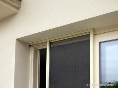Finestra scorrevole con telaio beige e pannello scuro sotto una parete color crema.