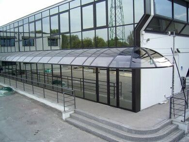 Edificio moderno con facciata in vetro, pensilina curva traslucida e scale esterne.