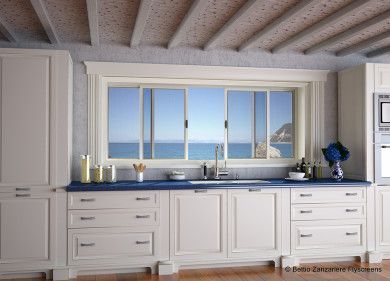 Luminosa cucina in stile costiero con mobili bianchi, piano di lavoro blu e ampia finestra con vista sull'oceano.
