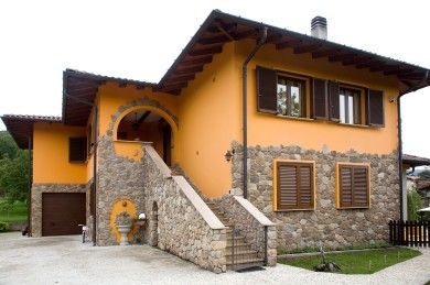 Casa in pietra e intonaco con pareti arancioni, scala esterna e persiane in legno.