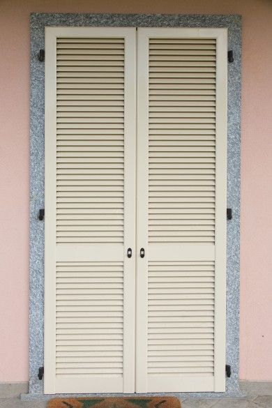 Doppie porte a persiana beige chiuse in una parete rosa con cornice in pietra grigia