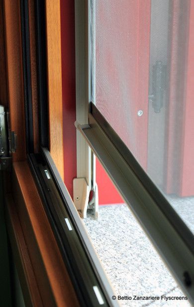 Finestra scorrevole parzialmente aperta, che mostra un muro esterno rosso e un piccolo gatto bianco che sbircia fuori.