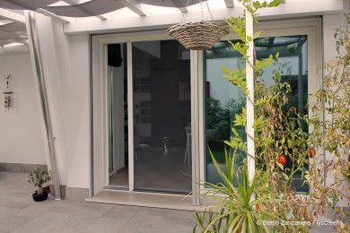 Porte scorrevoli in vetro che conducono a un patio, con un cesto appeso e piante in vaso ai lati.