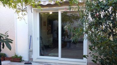 Porte finestre bianche incorniciate da piante, che si aprono su un luminoso cortile interno.