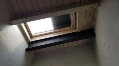 Lucernario aperto in un soffitto di legno inclinato con pareti bianche e una trave scura sottostante