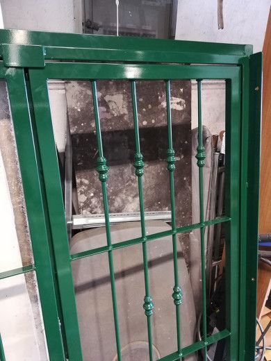 Cancello di sicurezza in metallo verde con sbarre decorative davanti a un muro.