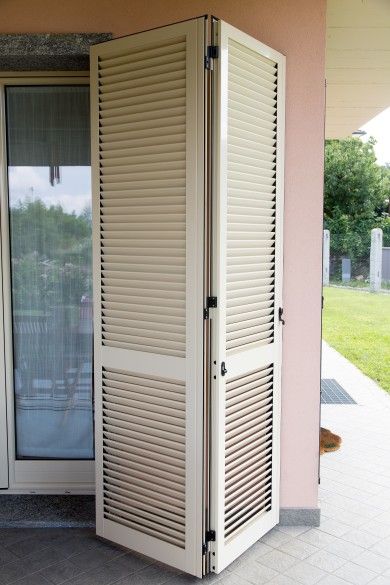 Armadio o mobiletto con ante a persiana di colore beige, posizionato su un patio piastrellato accanto a una porta scorrevole in vetro.