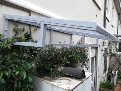 Una tenda grigia sovrasta la parete di un edificio, con fitti rampicanti verdi che ricoprono una piccola sporgenza sottostante.