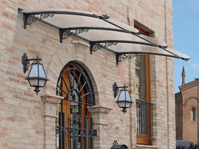 Facciata dell'edificio in pietra con finestra ad arco, lanterne nere e tenda da sole bianca sopra l'ingresso.