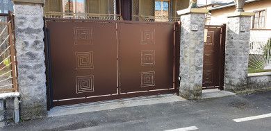 Cancello e porta laterale in metallo marrone incastonati in un muro di pietra lungo una strada residenziale