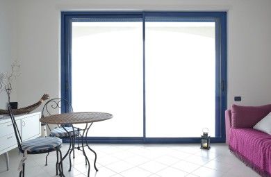 Soggiorno minimalista con porte scorrevoli in vetro blu, tavolo e sedie a sinistra, divano rosa a destra.