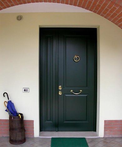 Porta d'ingresso verde scuro sotto un ingresso ad arco in mattoni, con un portaombrelli sulla sinistra.