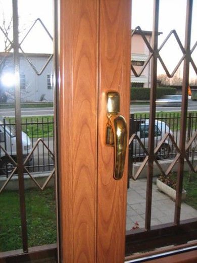 Porta d'ingresso in legno con maniglia in ottone e cancello di sicurezza, che si affaccia su un cortile al crepuscolo.