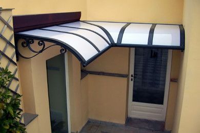 Tenda da sole curva bianca e nera sopra una porta e un piccolo patio tra pareti beige