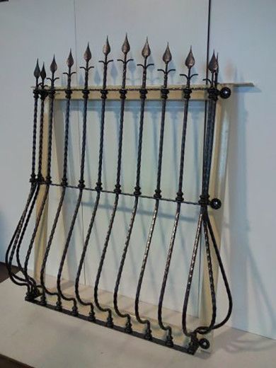 Parascintille in ferro battuto nero con pomelli decorativi a forma di lancia su una parete bianca.