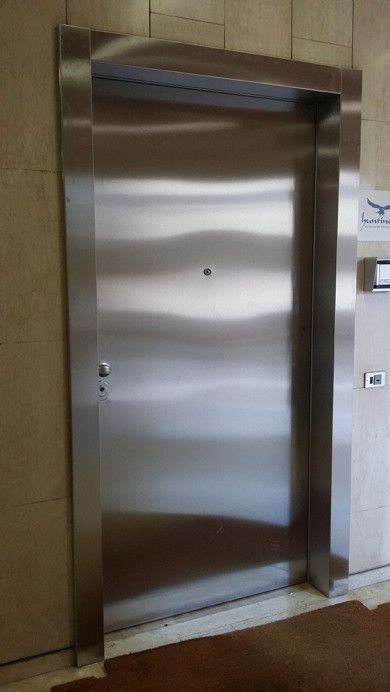 Porta dell'ascensore in acciaio inox in un corridoio piastrellato con pannello dei pulsanti di chiamata sulla destra.