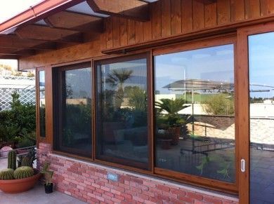 Porte scorrevoli in vetro con telaio in legno su un patio in mattoni con piante in vaso e tettoia.