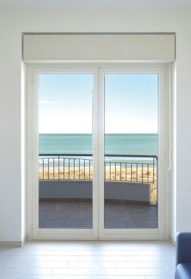 Porte scorrevoli in vetro che si aprono su un balcone con vista sull'oceano e sul cielo azzurro.