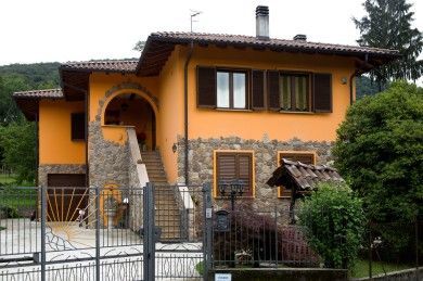 Casa arancione con arco in pietra, tetto di tegole e giardino recintato in un contesto rurale.
