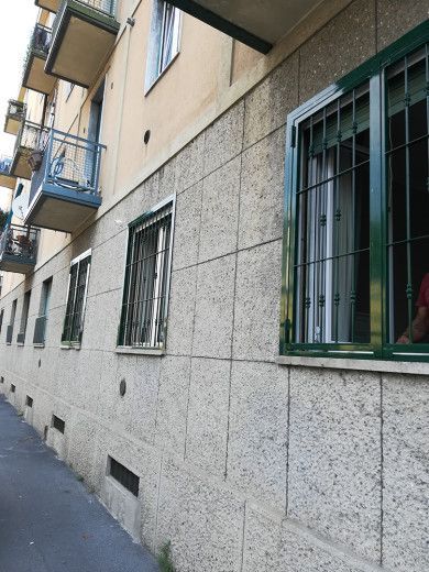 Stretta via accanto a un edificio beige con finestre e balconi con sbarre.
