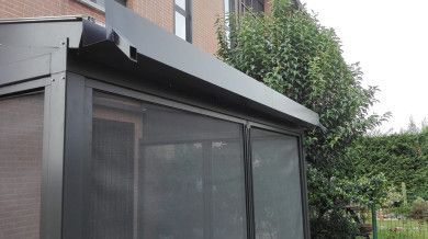 Tenda da sole nera sopra un patio schermato accanto a una casa in mattoni e vegetazione.