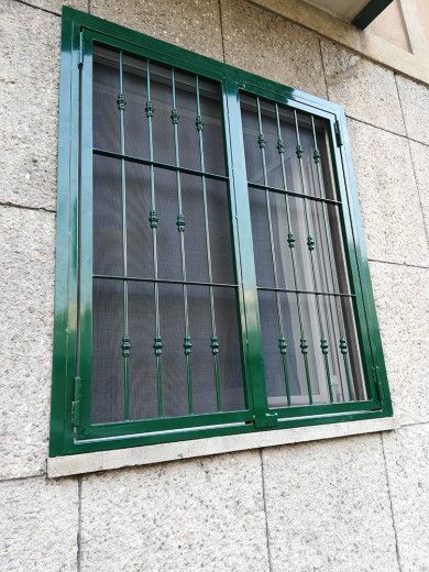 Finestra con inferriate di metallo verde su un muro di pietra.