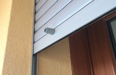Parete esterna con una piccola telecamera di sicurezza grigia montata sopra una porta.