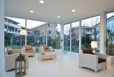 Soggiorno moderno con mobili bianchi, ampie finestre e vista su alberi ed edifici all'esterno.