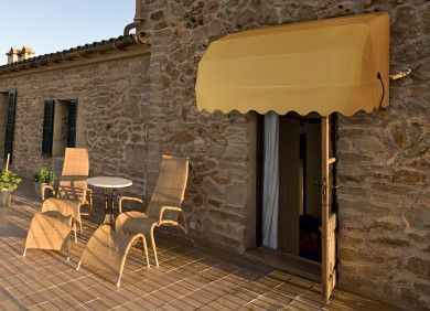 Patio in pietra con tenda da sole gialla, tavolo e sedie accanto a un edificio rustico.