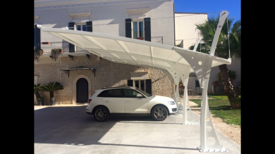 Un'auto bianca parcheggiata sotto una moderna tettoia bianca accanto a una casa beige in una giornata di sole.