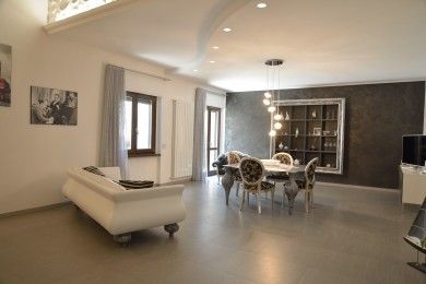 Soggiorno e sala da pranzo moderni a pianta aperta con divano bianco, tavolo e sedie, parete d'accento scura e lampade a sospensione.