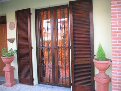 Ingresso principale con doppie porte marroni, cancello di sicurezza nero e piante in vaso su piedistalli in mattoni.
