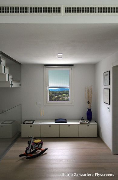Soggiorno minimalista con pareti bianche, finestra, mobile basso, vaso blu e un giocattolo sul pavimento.