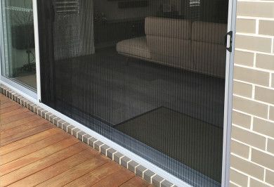 Porta scorrevole in vetro con zanzariera, che mostra un patio coperto e una terrazza in legno all'esterno.