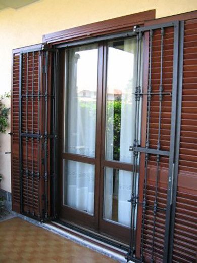 Persiane di legno marrone chiuse su una porta a vetri del balcone, dietro le quali si celano tende bianche.