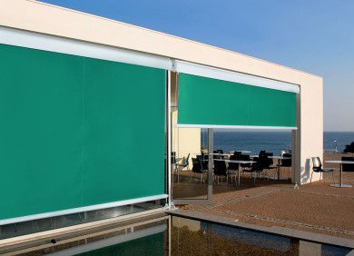 Edificio moderno con tende parasole color verde acqua che si affacciano sull'acqua e sul mare.