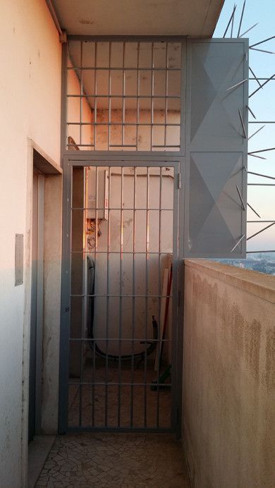 Stretto balcone dell'appartamento con cancello e sbarre di sicurezza in metallo, pareti beige e vista mare.