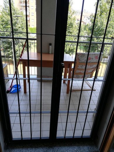 Cancello di sicurezza in metallo davanti a un balcone con tavolo, sedia e piante all'esterno.