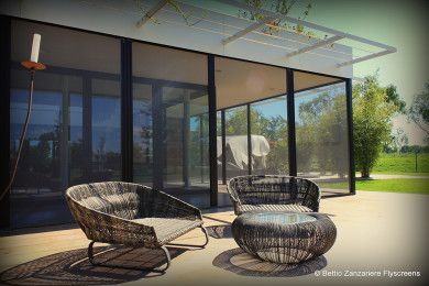 Patio moderno con sedie in vimini e tavolo rotondo accanto a una casa con pareti in vetro.