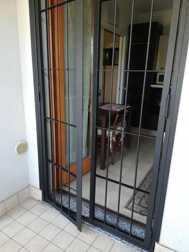 Cancello di sicurezza in metallo nero sopra una porta, con pavimento piastrellato e una stanza visibile all'interno.