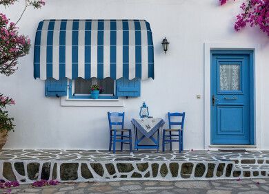 Tenda a righe blu e bianche sopra una porta blu e un tavolino da caffè con sedie su un muro bianco e un patio in pietra.