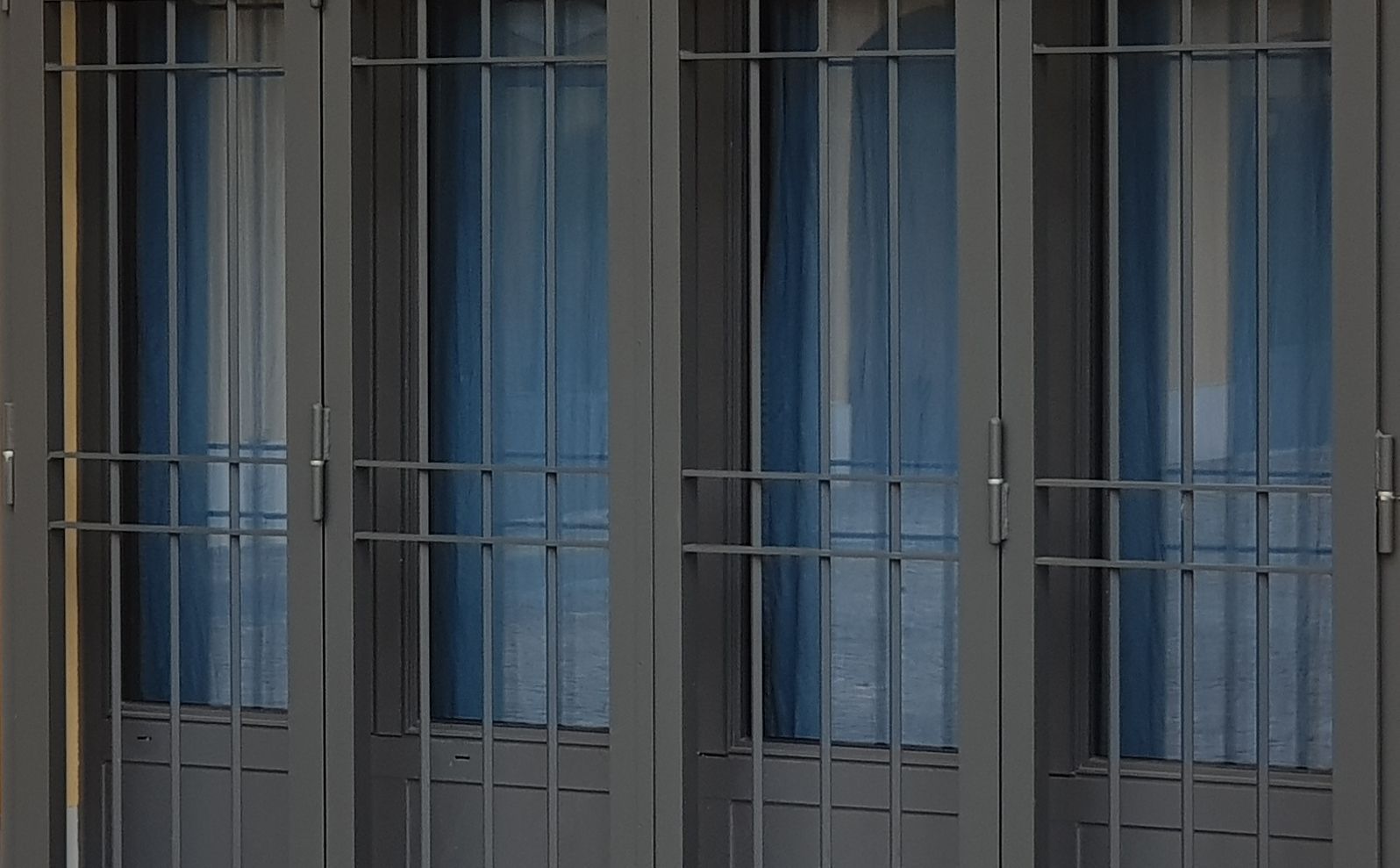 Inferriate di metallo grigio sopra vetri color blu sulla facciata di un edificio.