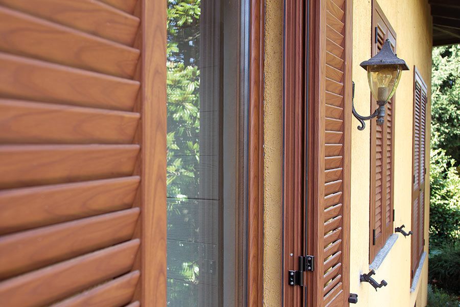 Persiane in legno e una porta sulla facciata di una casa gialla con una lanterna a muro.