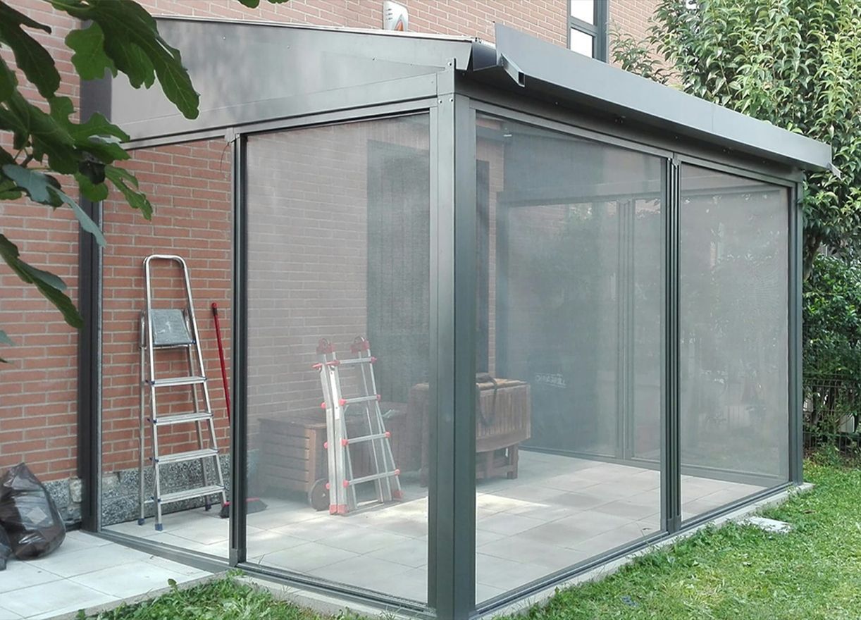 Veranda in vetro annessa a una casa in mattoni, con scale e attrezzi all'interno.