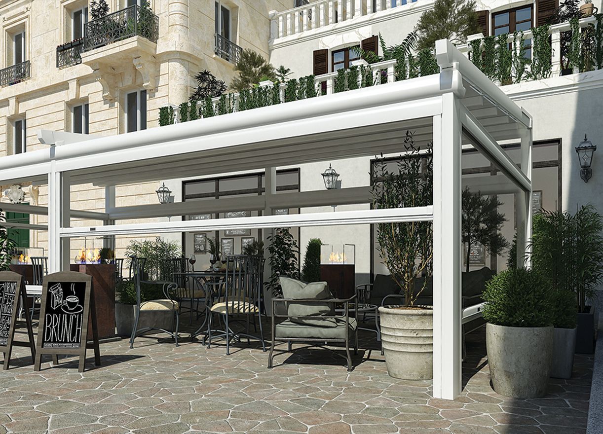 Dehor esterno di un caffè con pergola bianca, tavoli, sedie e piante in vaso, adiacente a un edificio.